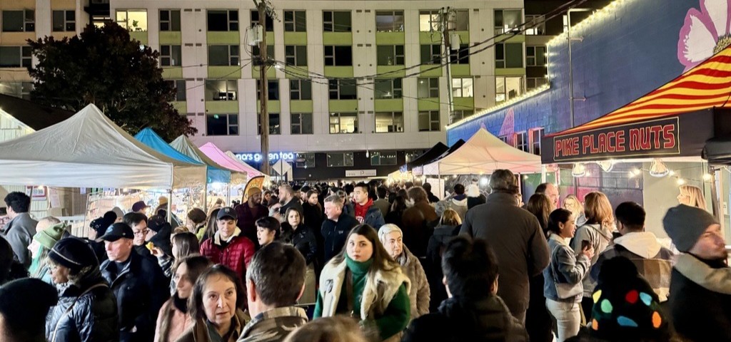 Crowd of people between two rows of canopies at a vibrant evening night market in Old Bellevue.