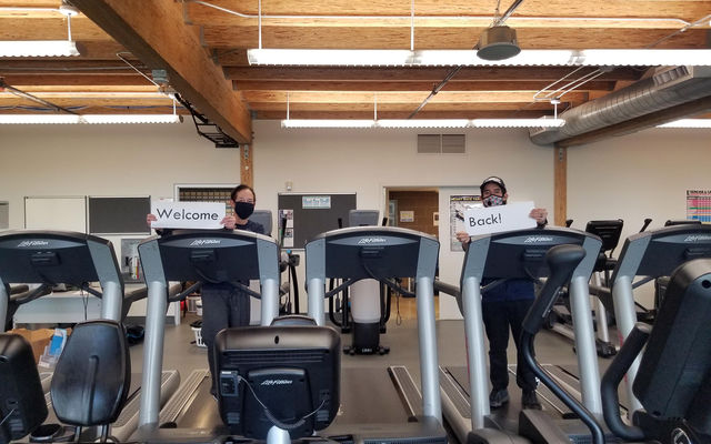Staff at the fitness center hold signs that together say, "Welcome back."