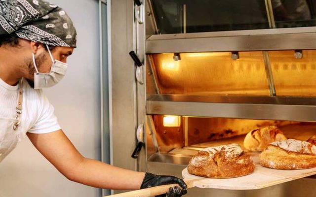 Image of worker taking bread out of commercial oven