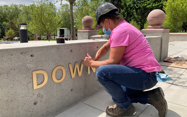 Kelli Lagerquist with Plumb Signs puts the finishing touches on the signage at Downtown Park’s new Northeast Gateway.
