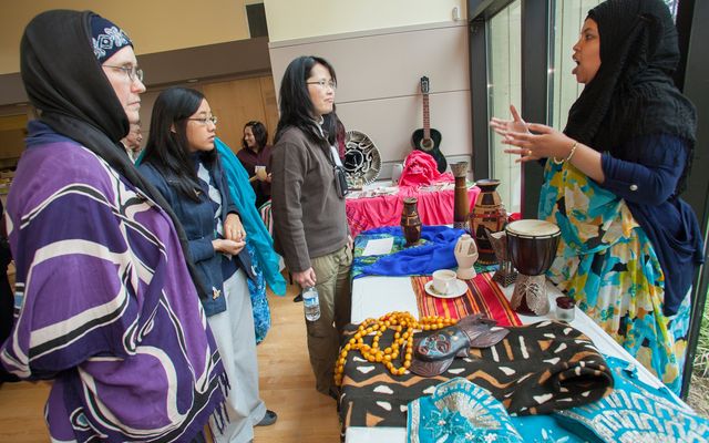 Women stop at a table where another women talks about her culture.