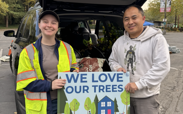 Happy residents pick up trees in October 2024 from the city's giveaway. They hold a yard sign that says, "We love our trees."