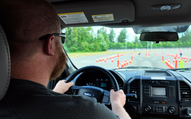 A man drives a truck on a parking lot with cones laid out in rows.