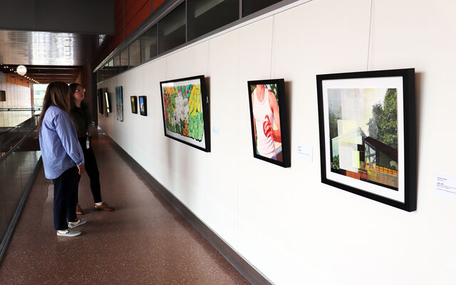 Two women look at paintings hanging in a City Hall corridor.