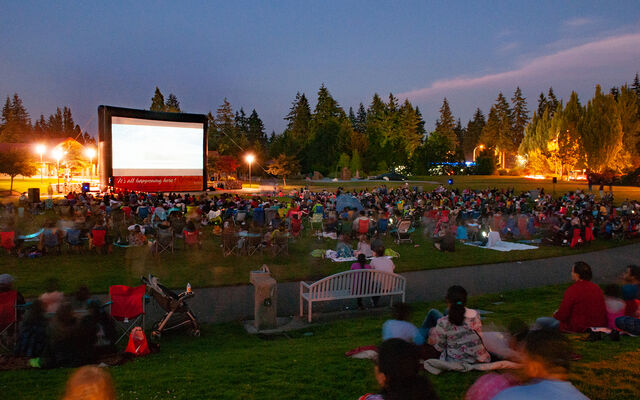 People sit on the grass at Crossroads Park and watch a movie on the big screen.