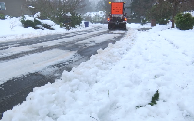 A snow plow truck driving down a curved road with snow build up on either side. 