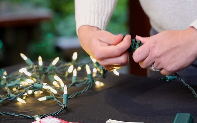 Two hands hold strings of holiday lights, one lit and one not.