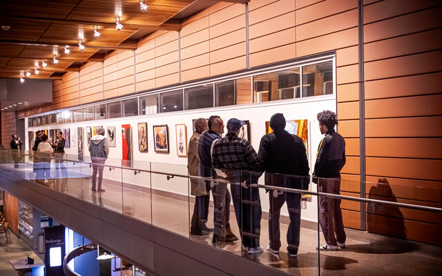 A group of people stand by a wall where paintings and other art hang.