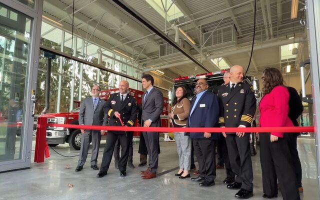 The mayor, deputy mayor and other councilmembers stand with the fire chief behind a red ribbon in the Fire Station 10 bay.