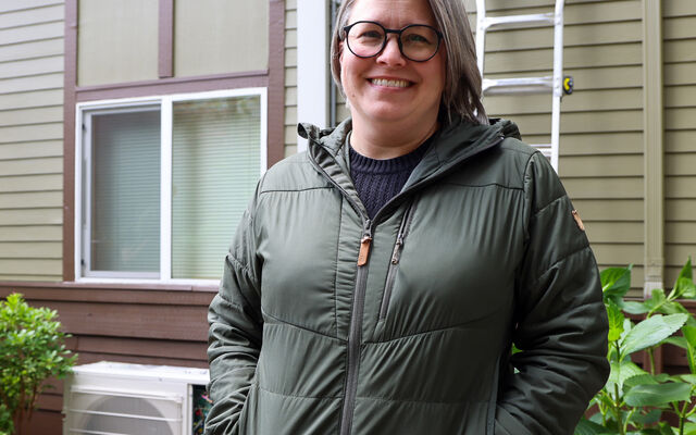 Jenni Treadway of Issaquah stands smiling in front of her new heat pump.