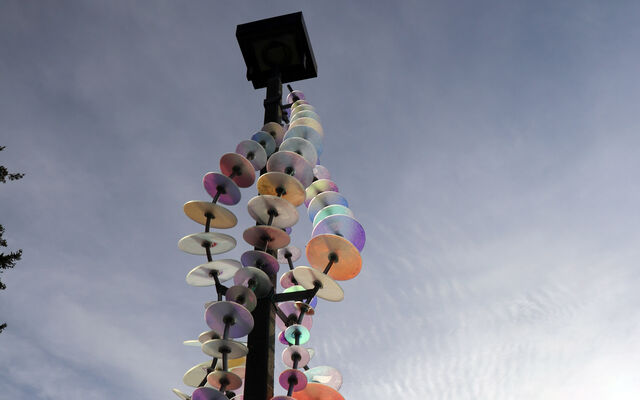 One of the installations that is part of "River" at Crossroads Park features colored glass disks threaded on metal wires draped around a light pole. lass