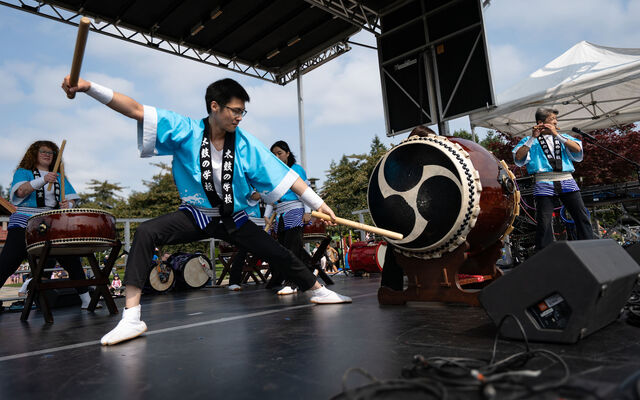 A man strikes a big taiko drum on a stage.