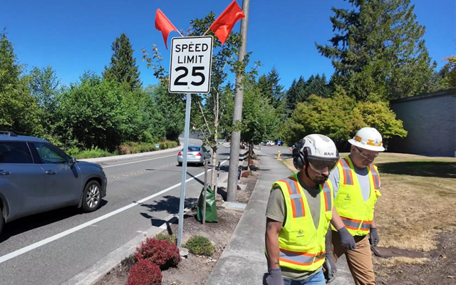 Workers walk away from a 25-mph speed limit sign they just installed by a Bellevue streeet.