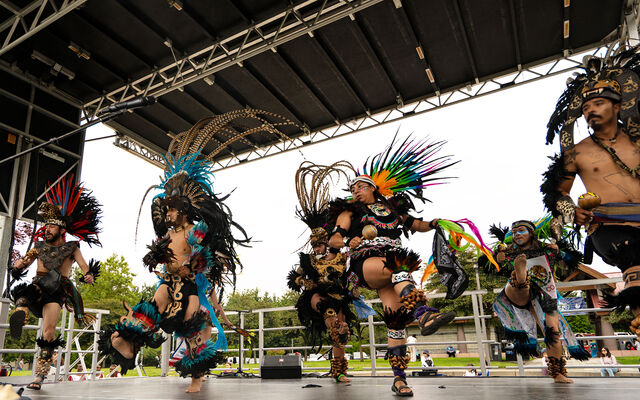 Danza Azteca performers dance in Aztec costumes on a stage at Crossroads Park.