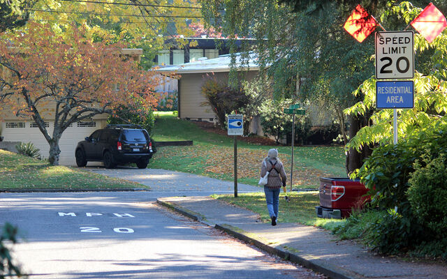 A woman walks on a sidewalk in the Surrey Downs neighborhood, past a sign advertising 20-mph speed limit.