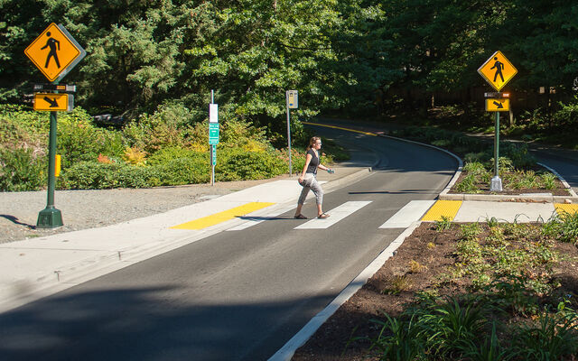 A woman walks in a crosswalk that has flashing beacons.