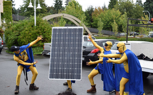 A crew installing solar panels on a Bellevue building stand with a panel in a parking lot dressed as superheroes.