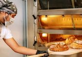Image of worker taking bread out of commercial oven