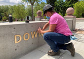 Kelli Lagerquist with Plumb Signs puts the finishing touches on the signage at Downtown Park’s new Northeast Gateway.
