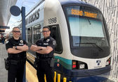 Officers Victor Pirak and Larry Perreira, members of the Bellevue Light Rail Unit (BLU), stand in front of a 2 Line train..