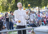 A man juggles three balls at Downtown Park while many people enjoy themselves behind him.