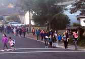 A large group of schoolchildren and parents walk in a procession down a neighborhood street and on a crosswalk.