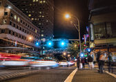 Cars and pedestrians cross an intersection in downtown Bellevue at night.