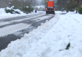 A snow plow truck driving down a curved road with snow build up on either side. 