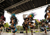 Danza Azteca performers dance in Aztec costumes on a stage at Crossroads Park.