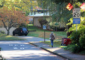 A woman walks on a sidewalk in the Surrey Downs neighborhood, past a sign advertising 20-mph speed limit.