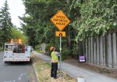 A Transportation worker installs a sign next to a street that reads "speed enforced ahead."