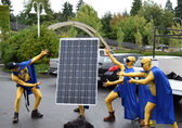 A crew installing solar panels on a Bellevue building stand with a panel in a parking lot dressed as superheroes.