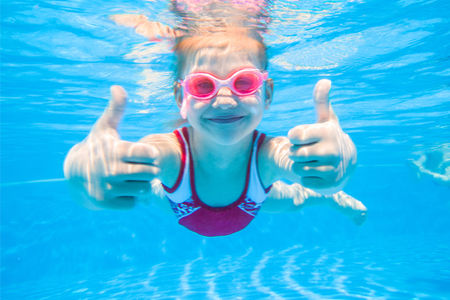 Girl showing thumbs up under water in a pool