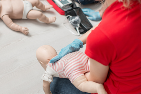 Image of a white woman holding an infant CPR mannequin while practicing choking interventions. 