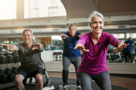 Mature group squat for exercise in gym.