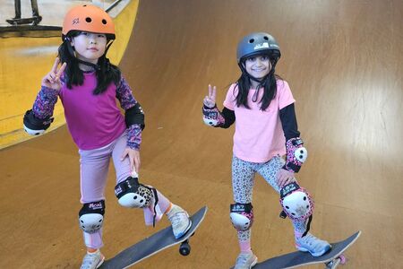 two young girls on skateboard, smile and pose for photo