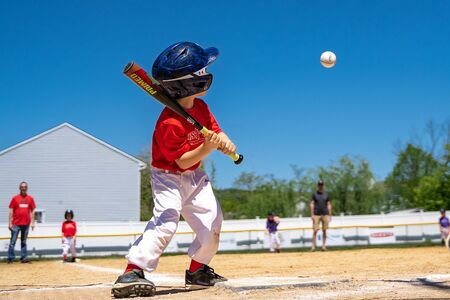 Young child on baseball field swings bat to hit baseball