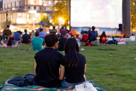Two people sitting in Downtown Park in front of large movie screen