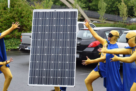 Staff dressed in superhero costumes show off a solar panel in a parking lot.