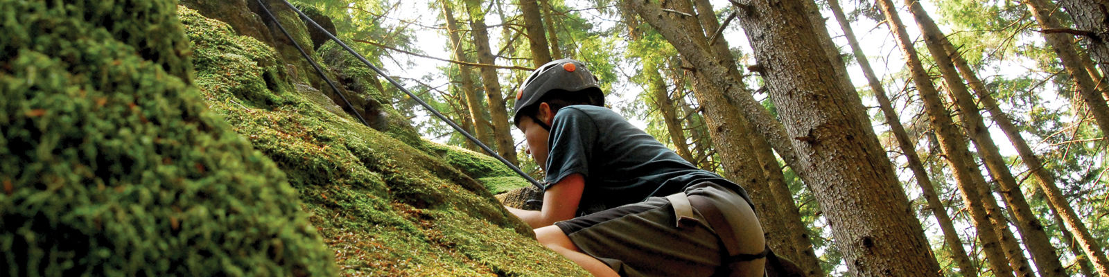 A boy climbing a mossy cliff in the woods