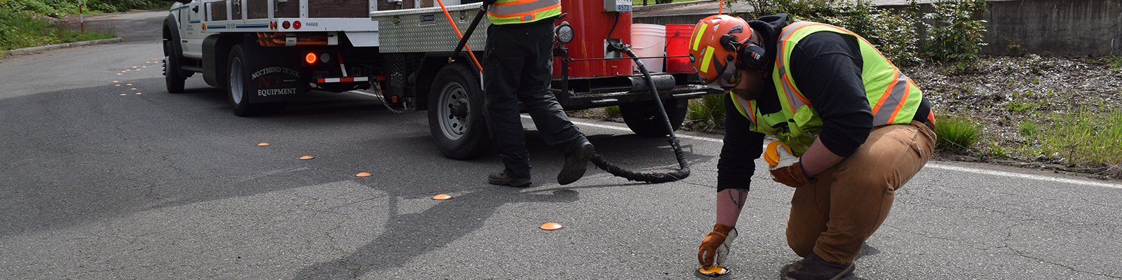 An image of transportation staff applying road pavement marker for center lane channelization with hot tar.