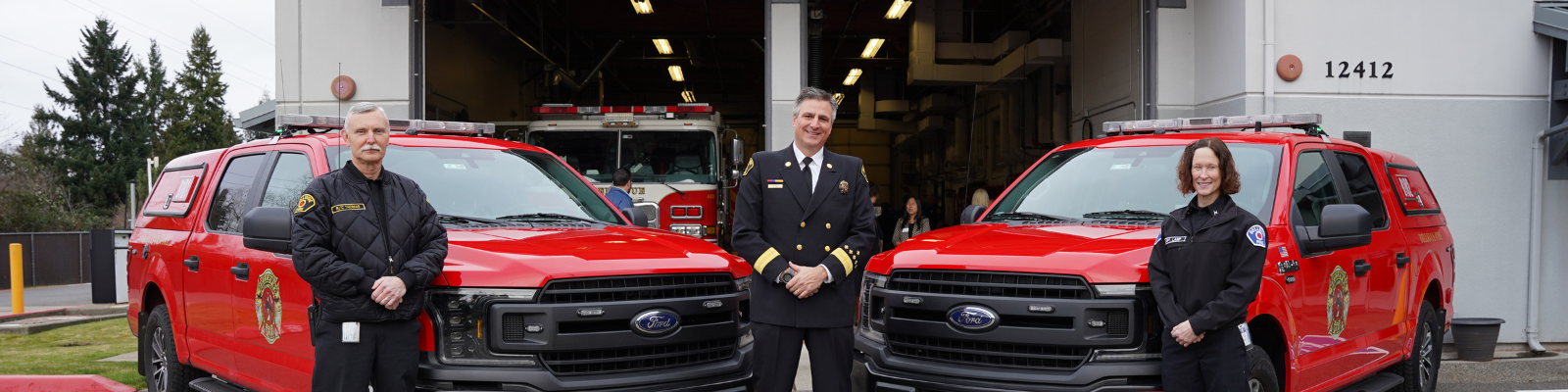 Image of Bellevue Fire Chief standing in between two fire department battalion chiefs and their red pickup trucks. 
