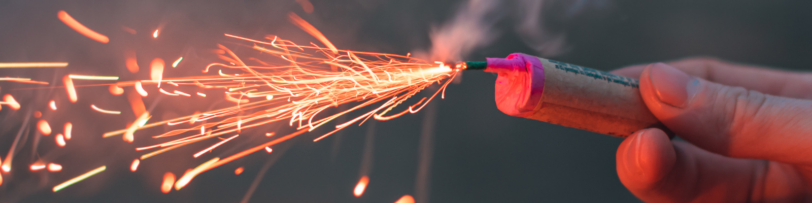 Close up image of a hand holding a firework with sparks coming out of the end.