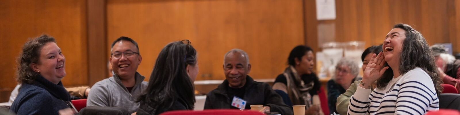 Photo of people sitting around a table talking and laughing from a Cultural Conversations event.