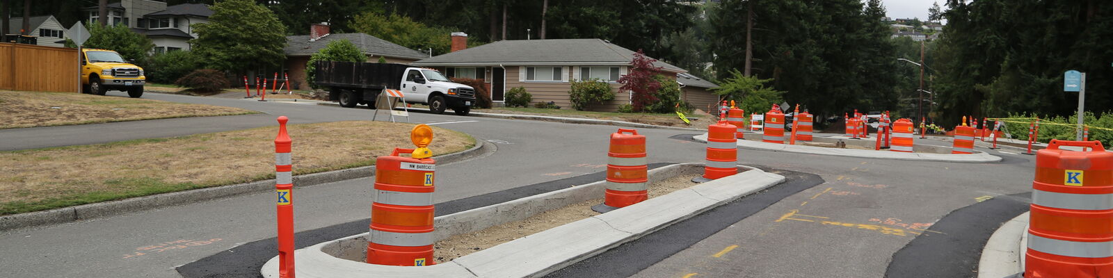 Two lane road with traffic cones. There is a center median with a roundabout in background.