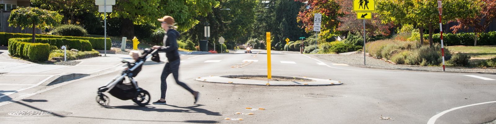 Image of person pushing a baby stroller through an intersection with a traffic circle 