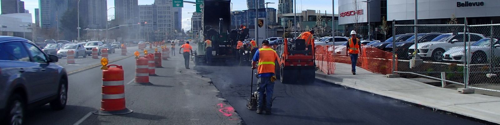 Image of crew repaving street with new asphalt -- downtown skyline in background