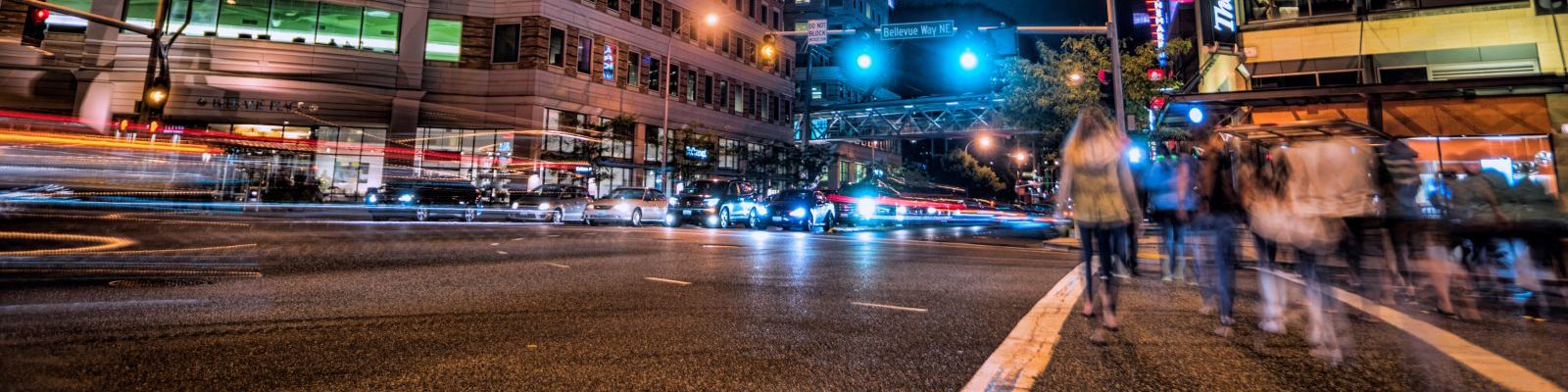 Image of pedestrians at night in a downtown crosswalk with cars nearby