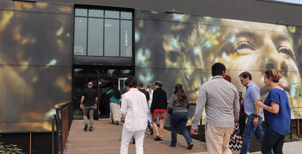 People walking into Porchlight men's shelter building. Mural of person's face on side of building.
