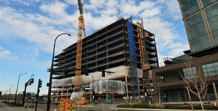 A multi-story building is partially constructed and still in construction phase with no exterior walls. A crane is in the foreground. 